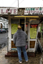 A woman is standing over a street shop. The owner explains on a note she supports the protests but needs to work as she is a single mom.